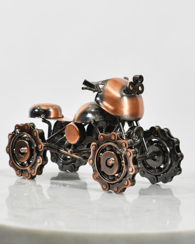 Puede incluir: Una peque&ntilde;a escultura de motocicleta de metal de color cobre con detalles negros. La motocicleta tiene cuatro ruedas hechas de cadenas unidas.