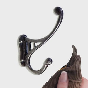 May include: A dark grey metal coat hook with a curved design. The hook features a decorative ball at the top and bottom of the curved section. A brown corduroy fabric is partially visible, suggesting the hook is in use.