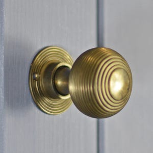 May include: A brass door knob with a round, ribbed design. The knob is attached to a round, decorative plate.