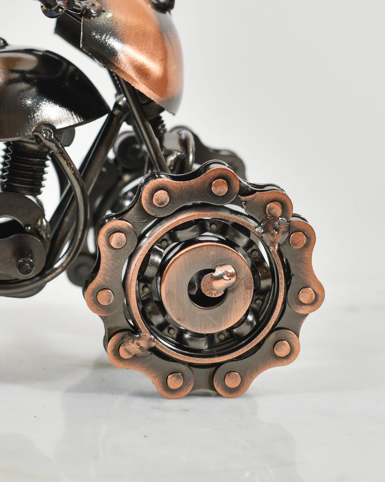 Puede incluir: Una escultura de motocicleta de metal con acabado de cobre. La motocicleta tiene una transmisi&oacute;n por cadena y un motor detallado.