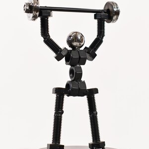 May include: A black metal sculpture of a person lifting weights. The sculpture is made of nuts and bolts and is standing on a black metal base.