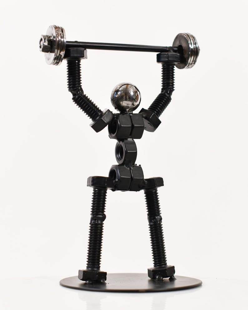 May include: A black metal sculpture of a person lifting weights. The sculpture is made of nuts and bolts and is standing on a black metal base.