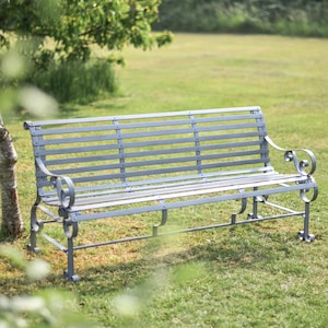 May include: A grey metal garden bench with a slatted design and ornate scrollwork on the ends. The bench is sitting on a grassy lawn.