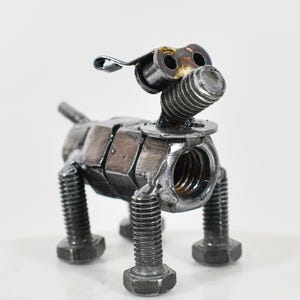 May include: A metal dog sculpture made from nuts, bolts, and other hardware. The dog features a bolt for a nose and a curved metal piece for an ear. This quirky sculpture is a unique piece of art, perfect for a home or office.