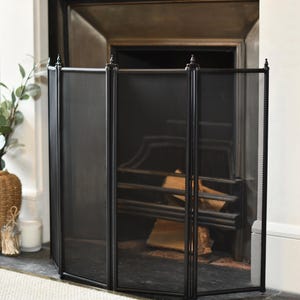 May include: Black metal fireplace screen with a mesh design. The screen is made up of four panels that fold out to create a barrier around the fireplace.