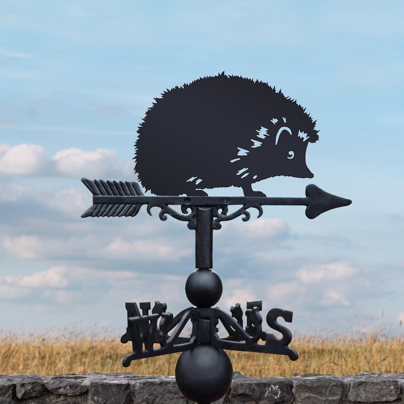 May include: Black metal weather vane featuring a silhouette of a hedgehog. The vane is mounted on a post and has four directional arrows.
