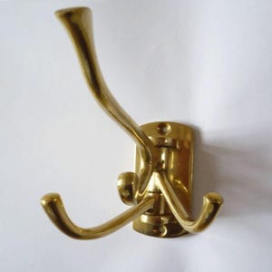 May include: A brass coat hook with three hooks. The hook is mounted on a rectangular base.