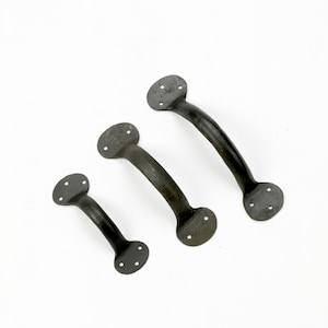 May include: Three black metal door handles of different sizes. The handles are curved and have rounded ends with four holes for mounting.