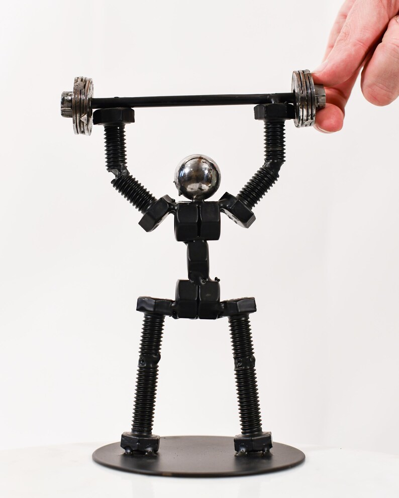 May include: A black metal sculpture of a person lifting a barbell. The sculpture is made of nuts and bolts and is standing on a black base.