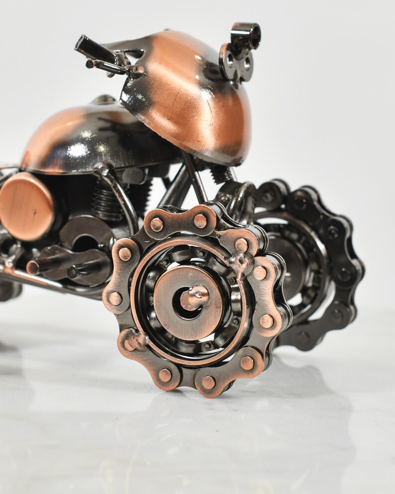 Puede incluir: Una peque&ntilde;a escultura de motocicleta de metal hecha con piezas recicladas. La motocicleta es de color negro y cobre y tiene una transmisi&oacute;n por cadena.