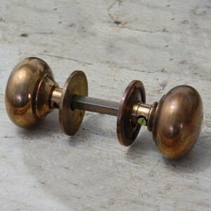 May include: A pair of antique brass door knobs with a round shape and a simple design. The knobs are attached to a metal rod.