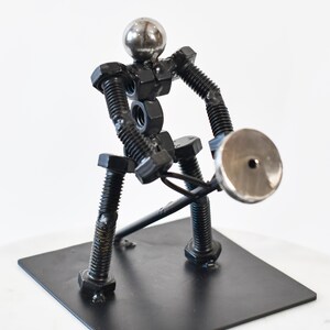 May include: A metal sculpture of a person lifting a weight. The sculpture is made of nuts, bolts, and other metal pieces. The person is standing on a black metal base.