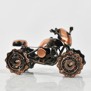 Puede incluir: Una peque&ntilde;a escultura de motocicleta de color cobre hecha de engranajes y cadenas de metal. La motocicleta tiene un dise&ntilde;o detallado y es una obra de arte &uacute;nica.