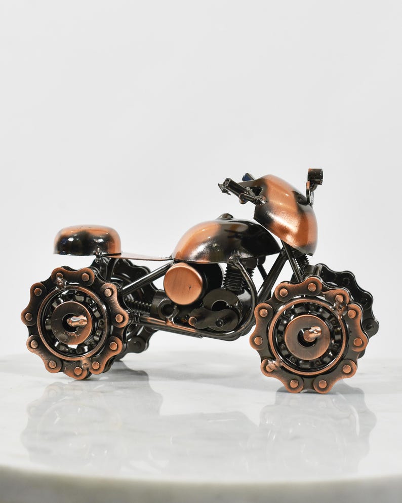 Puede incluir: Una peque&ntilde;a escultura de motocicleta de color cobre hecha de engranajes y cadenas de metal. La motocicleta tiene un dise&ntilde;o detallado y es una obra de arte &uacute;nica.
