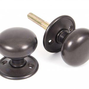 May include: Dark bronze door knobs with matching backplates and a connecting bolt. The knobs have a rounded shape, and the backplates are circular with screw holes. The hardware is set against a white background.