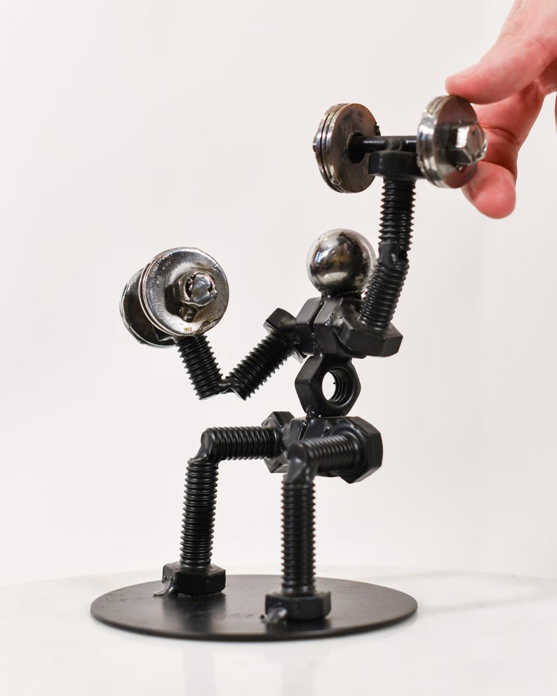 May include: A metal sculpture of a person lifting weights. The sculpture is made of nuts, bolts, and washers. The person is sitting on a round metal base.