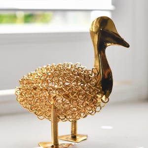 May include: A gold metal duck sculpture made of wire. The duck has a detailed body and a long neck.
