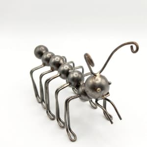 May include: A metal ant sculpture with a segmented body and curved legs. The ant's body is formed from small, round metal balls, and its antennae curve upwards. The sculpture is set against a white backdrop.