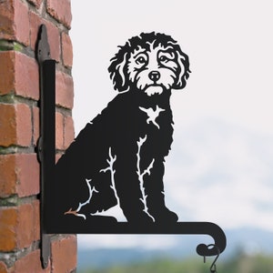 May include: Black metal silhouette of a sitting dog with curly hair, mounted on a bracket for hanging on a wall.
