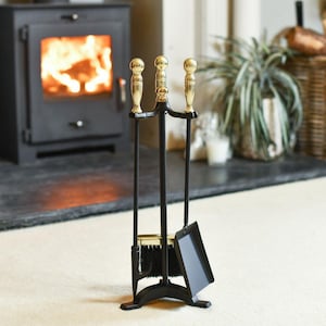 May include: A black fireplace tool set featuring a stand with three upright rods topped with polished brass spherical finials. The set includes a shovel, a brush with black bristles, and a poker, all suspended from the central metal frame.