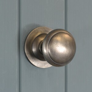 May include: A silver door knob with a round, slightly raised design. The knob is mounted on a silver plate.