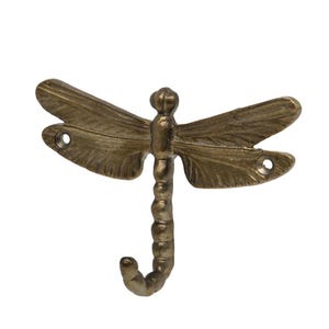 May include: A bronze dragonfly hook. The hook is shaped like a dragonfly with detailed wings and a curved hook at the bottom. The dragonfly has a textured body and wings, designed for wall mounting.