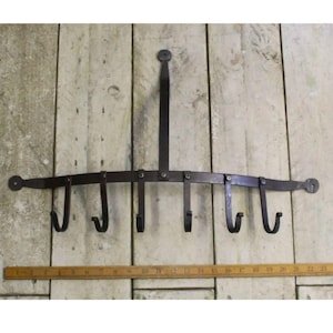 May include: A black metal pot rack with six hooks. The rack is mounted to a wooden wall and has a curved design.