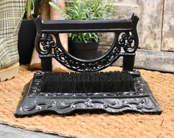 May include: Black cast iron boot scraper with a brush and ornate design. The scraper is on a brown coir doormat.