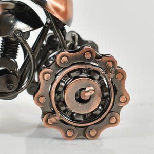 Puede incluir: Una escultura de motocicleta de metal con acabado de cobre. La motocicleta tiene una transmisi&oacute;n por cadena y un motor detallado.