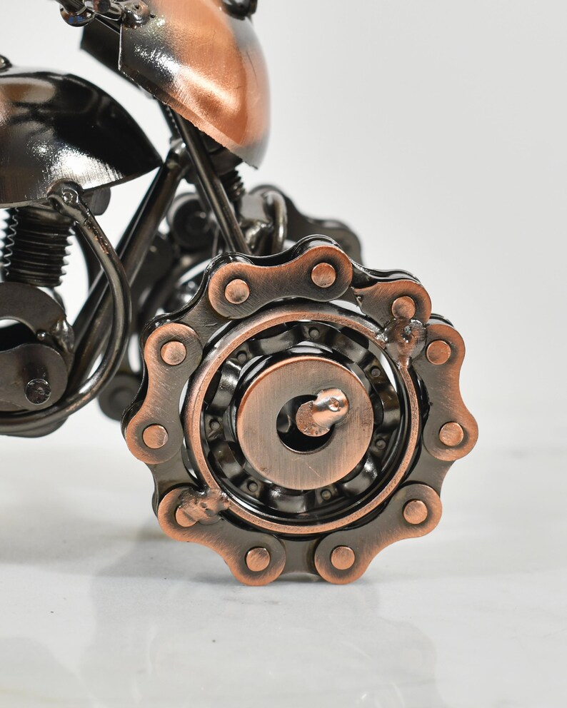 Puede incluir: Una escultura de motocicleta de metal con acabado de cobre. La motocicleta tiene una transmisi&oacute;n por cadena y un motor detallado.