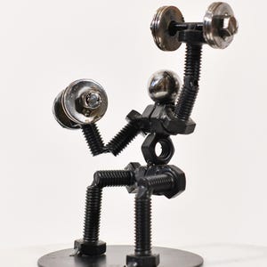 May include: A metal sculpture of a person lifting weights. The sculpture is made of nuts, bolts, and washers. The person is sitting on a round base.