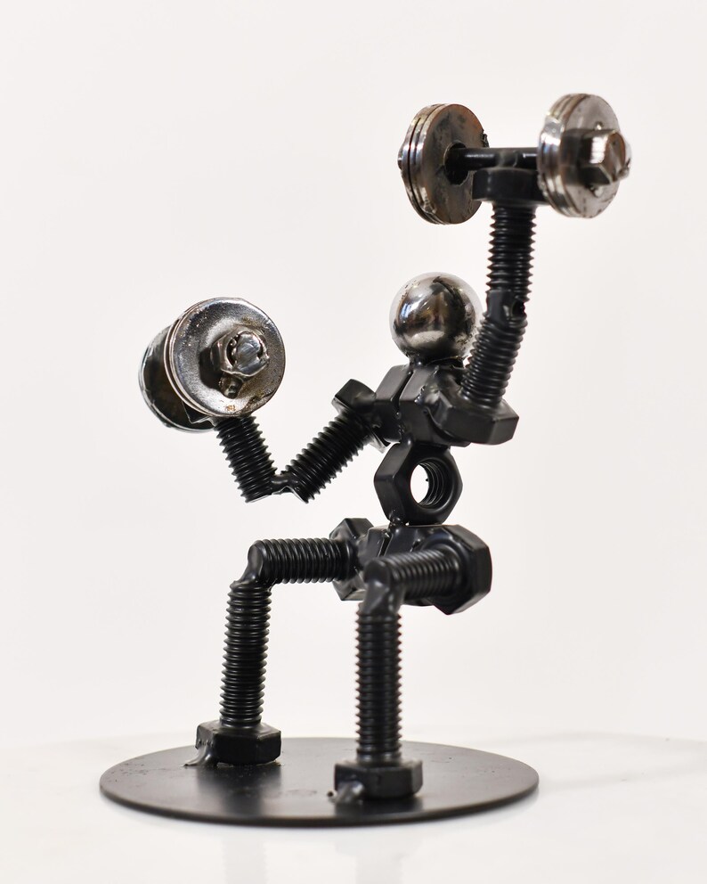 May include: A metal sculpture of a person lifting weights. The sculpture is made of nuts, bolts, and washers. The person is sitting on a round base.