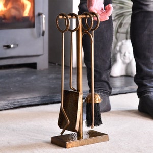 May include: A set of four antique gold fireplace tools with a hammered finish. The tools include a poker, shovel, tongs, and a brush. The tools are mounted on a stand with a hammered finish.