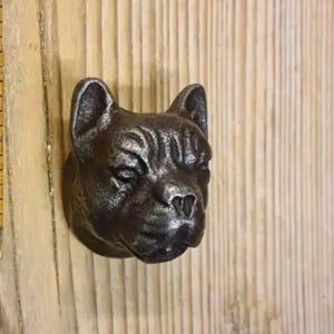 May include: A cast iron dog head door knocker in a dark grey finish. The dog has a wrinkled face and a slightly open mouth.