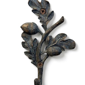 May include: A bronze-effect metal wall hook in the shape of an oak branch, complete with leaves and acorns. The hook is secured with two screws. The finish has a distressed, antique look, giving it a rustic feel.