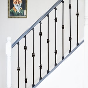 May include: Black metal stair railing with round finials. The railing is attached to a white wall and a white painted wooden post.