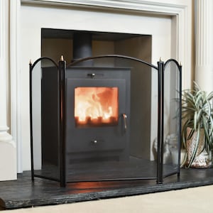 May include: Black metal fireplace screen with three panels and gold accents. The screen is in front of a wood-burning stove with a fire burning inside.