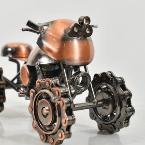 Puede incluir: Una peque&ntilde;a motocicleta decorativa hecha de metal. La motocicleta est&aacute; pintada en color cobre y tiene ruedas de metal negro con detalles de cadena. La motocicleta es una r&eacute;plica en miniatura de una motocicleta real.