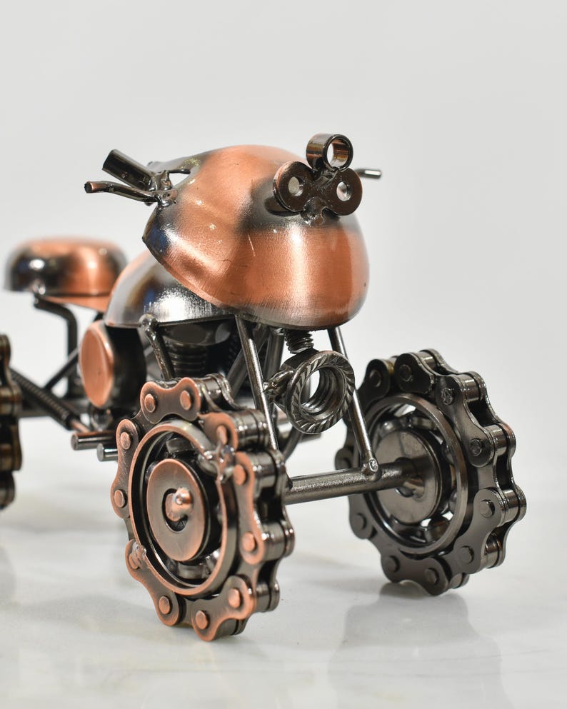 Puede incluir: Una peque&ntilde;a motocicleta decorativa hecha de metal. La motocicleta est&aacute; pintada en color cobre y tiene ruedas de metal negro con detalles de cadena. La motocicleta es una r&eacute;plica en miniatura de una motocicleta real.