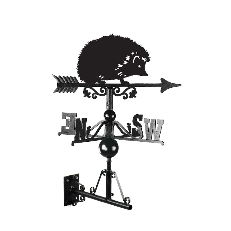 May include: Black metal hedgehog weather vane with a compass rose and the directions N, E, S, and W. The vane is mounted on a black metal bracket.
