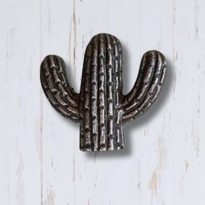 May include: A silver metal cactus shaped door knob or pull. The cactus has a textured surface and is a popular southwestern style home decor item.