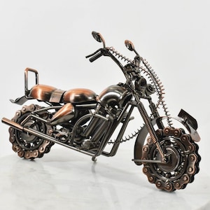 May include: A decorative motorcycle sculpture crafted from dark metal and copper-toned components. The model features wheels made from gear chains, a coiled spring front fork, handlebars with mirrors, and a smooth, rounded fuel tank and seat.