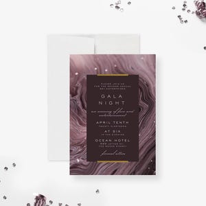 May include: An invitation for a Gala Night event. The invitation features a dark brown rectangular text box with gold accents, containing event details. The background has a swirling, abstract design in shades of purple and white. The invitation is placed on a white surface.