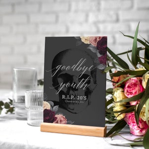 May include: A black and white skull graphic with floral accents on a black background. The text "goodbye youth" and "R.I.P. 20's Cheers to my 20's" is printed on the sign.