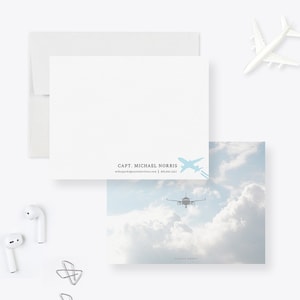 May include: A white card with a blue airplane silhouette and the text "CAPT. MICHAEL NORRIS" and contact information. The card is on a white background with a blue sky and white clouds in the background.