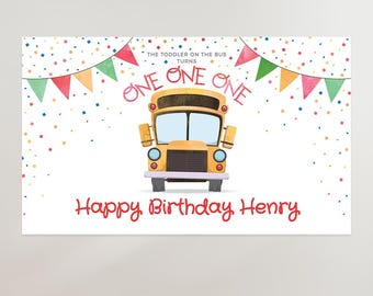 Könnte beinhalten: Ein weißes, rechteckiges Geburtstagsschild mit einer gelben Schulbus-Illustration in der Mitte. Der Text lautet: THE TODDLER ON THE BUS TURNS ONE ONE ONE und Happy Birthday Henry. Bunte Wimpelketten und Konfetti verzieren den Hintergrund.
