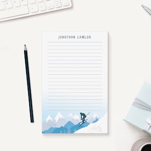 May include: A blue and white notepad with a skier silhouette on the bottom. The notepad has lined paper and the name "JONATHAN LAWLOR" printed at the top.