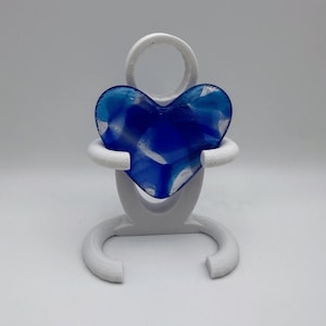 Peut inclure: Une sculpture abstraite blanche tenant un objet en forme de cœur bleu. Le cœur est en verre translucide avec des nuances de bleu et de blanc. La sculpture a un design minimaliste, avec un sommet circulaire et une base incurvée.