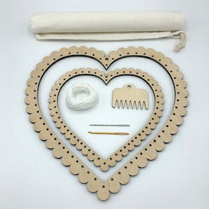 May include: A heart-shaped wooden embroidery hoop kit with two hoops, white yarn, a comb, and two needles. The kit comes with a white fabric bag.