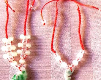 May include: Two adjustable bracelets featuring vibrant red cord strings. The left bracelet displays a cluster of clear and opaque white beads with a green and white stone pendant. The right bracelet features a single green and white stone pendant.